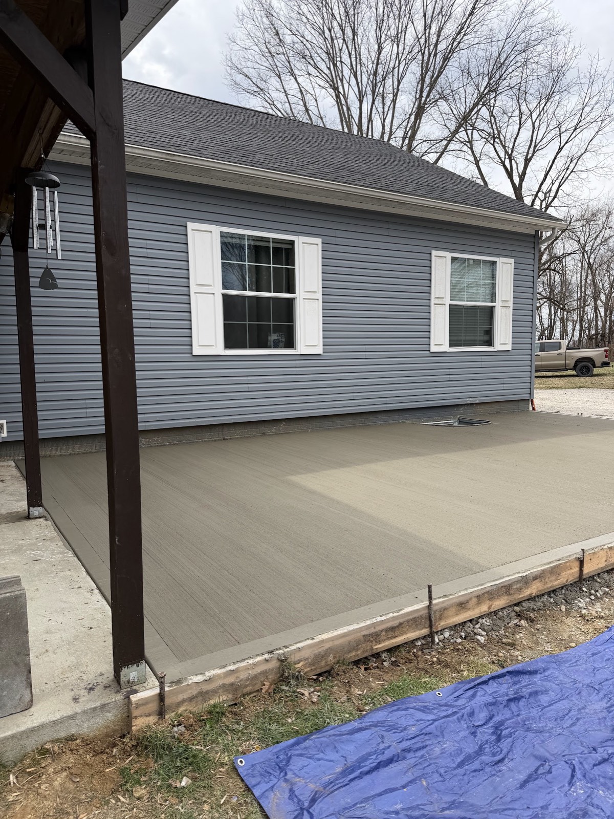 Freshly poured and broom-finished concrete patio with wood forms still in place beside a blue-sided house.