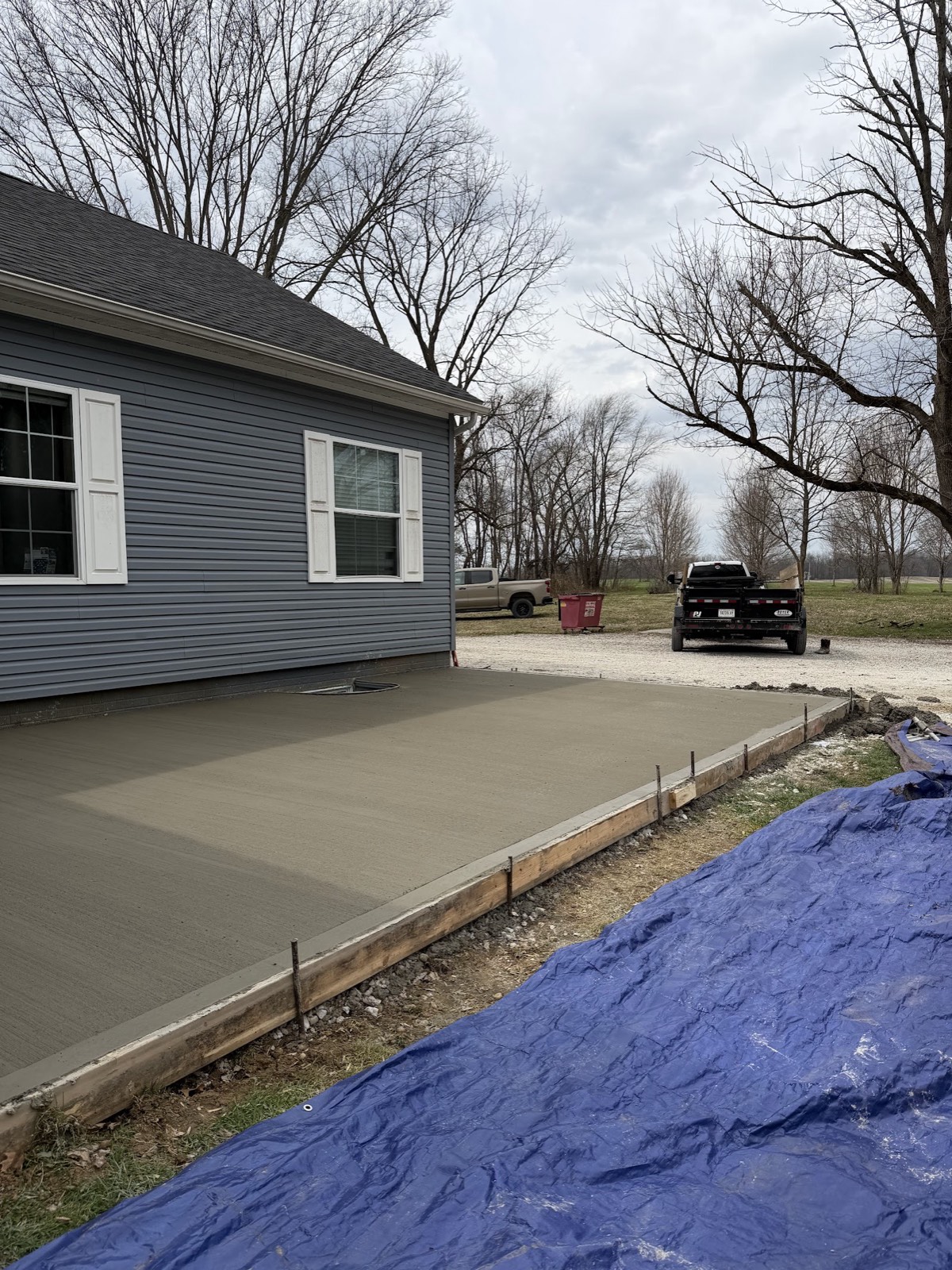 Freshly finished broom-textured concrete patio still in its forms beside a blue-gray house.