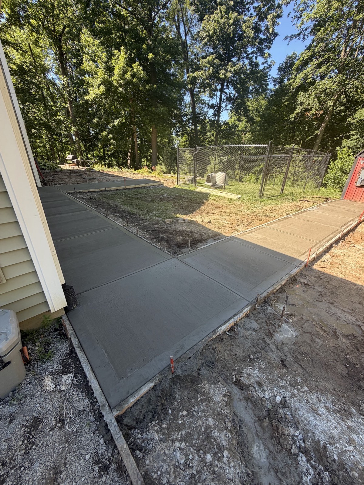 Freshly finished concrete sidewalk and pads still in forms, wrapping around a house toward a fenced backyard.