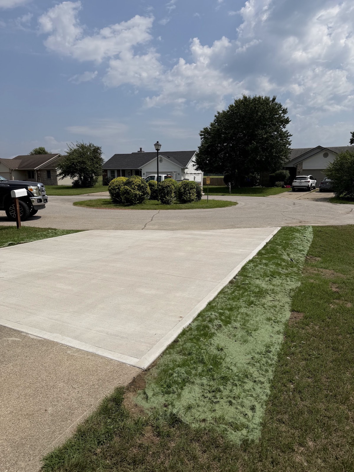 Newly poured concrete driveway pad with hydroseeded strip along the edge in a cul-de-sac neighborhood.