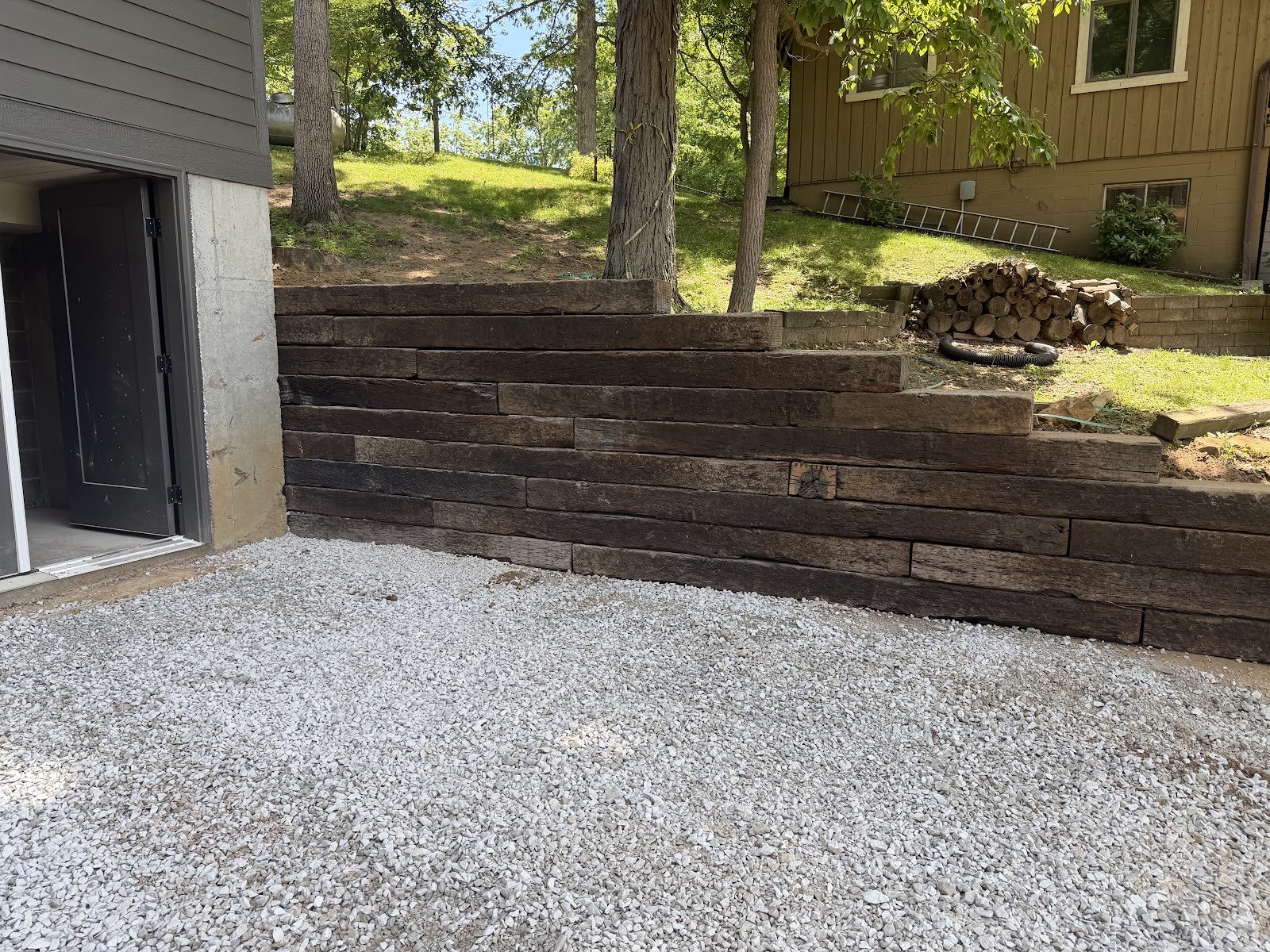 Stepped railroad-tie retaining wall above a new white gravel patio area at a walkout basement.