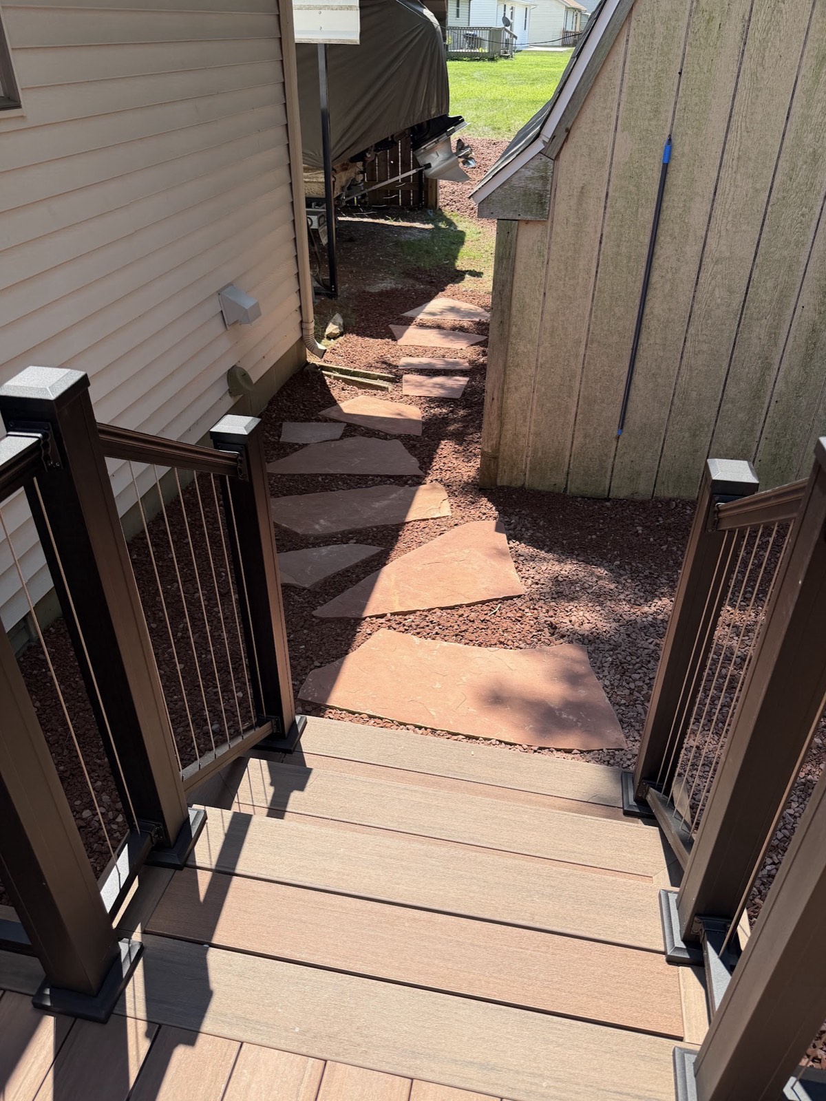 Flagstone stepping-stone path set in red gravel leading from new composite deck stairs between buildings.