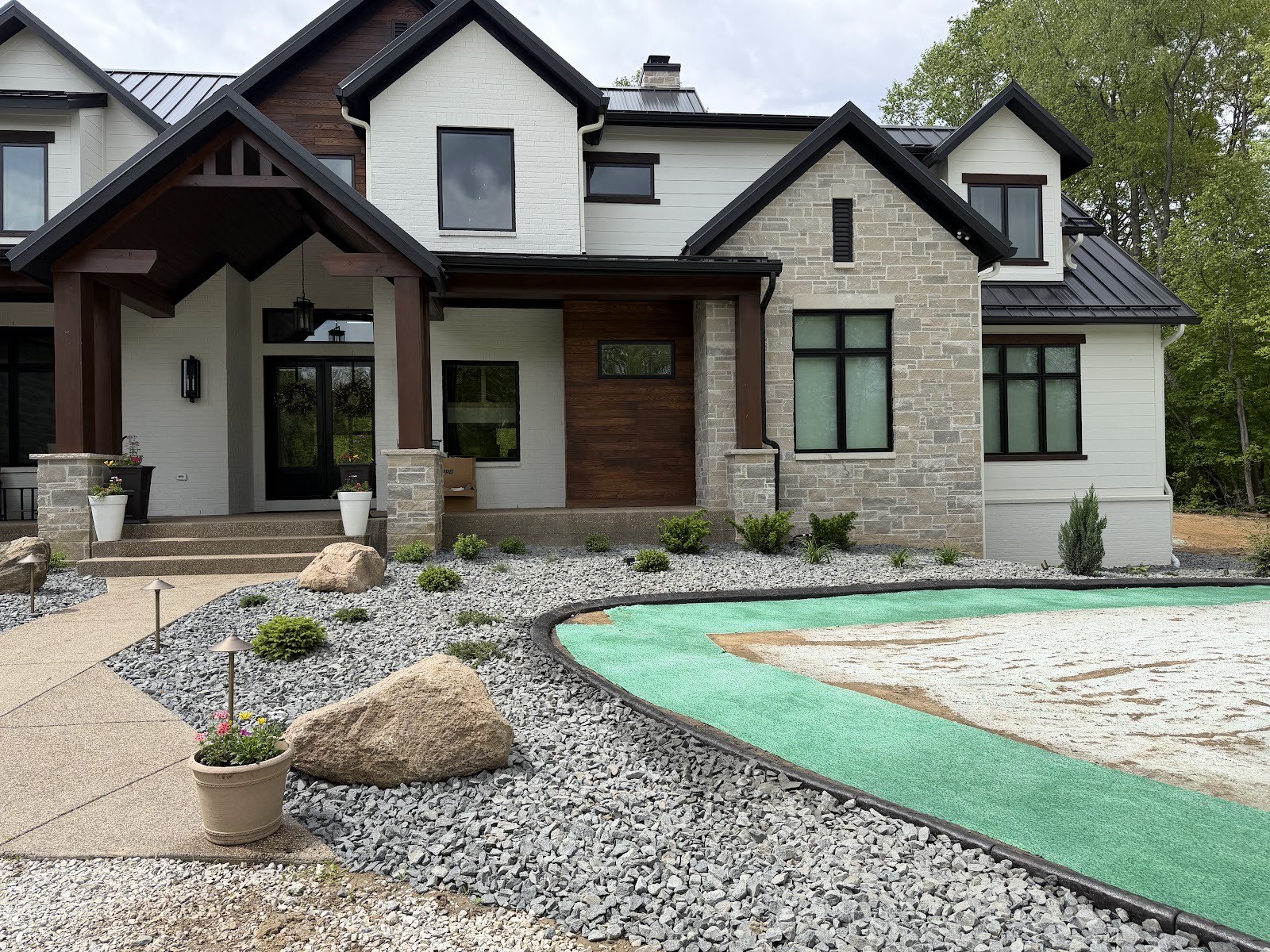 Front elevation of an upscale modern farmhouse with completed gravel beds, boulders, plantings, and fresh hydroseed lawn.