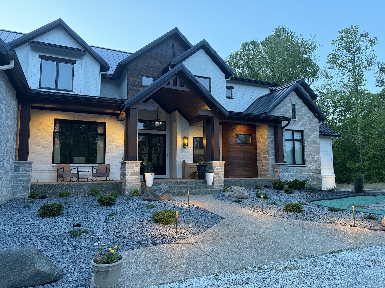 Dusk shot of a finished modern farmhouse with gravel beds, boulders, shrubs, and low-voltage landscape lighting along the front walk.