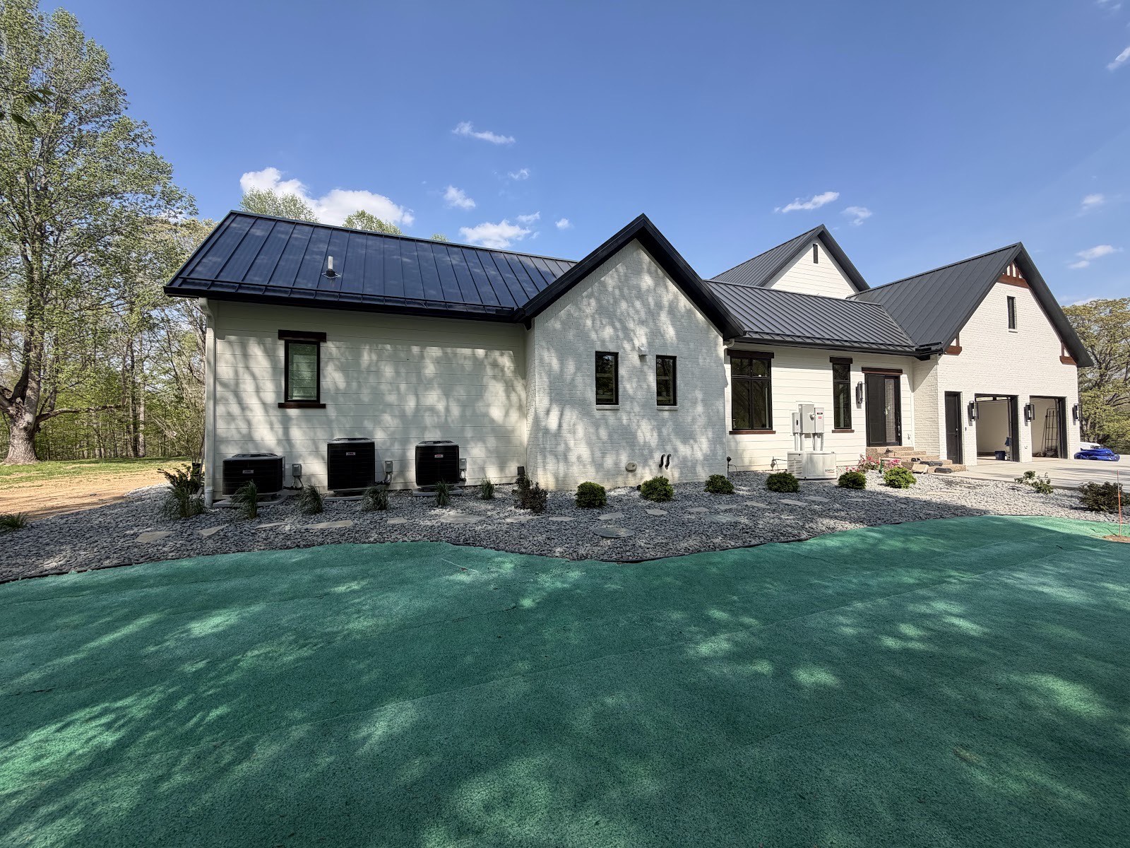Freshly hydroseeded lawn and gray gravel foundation beds with steppers around a white modern farmhouse on a sunny day.