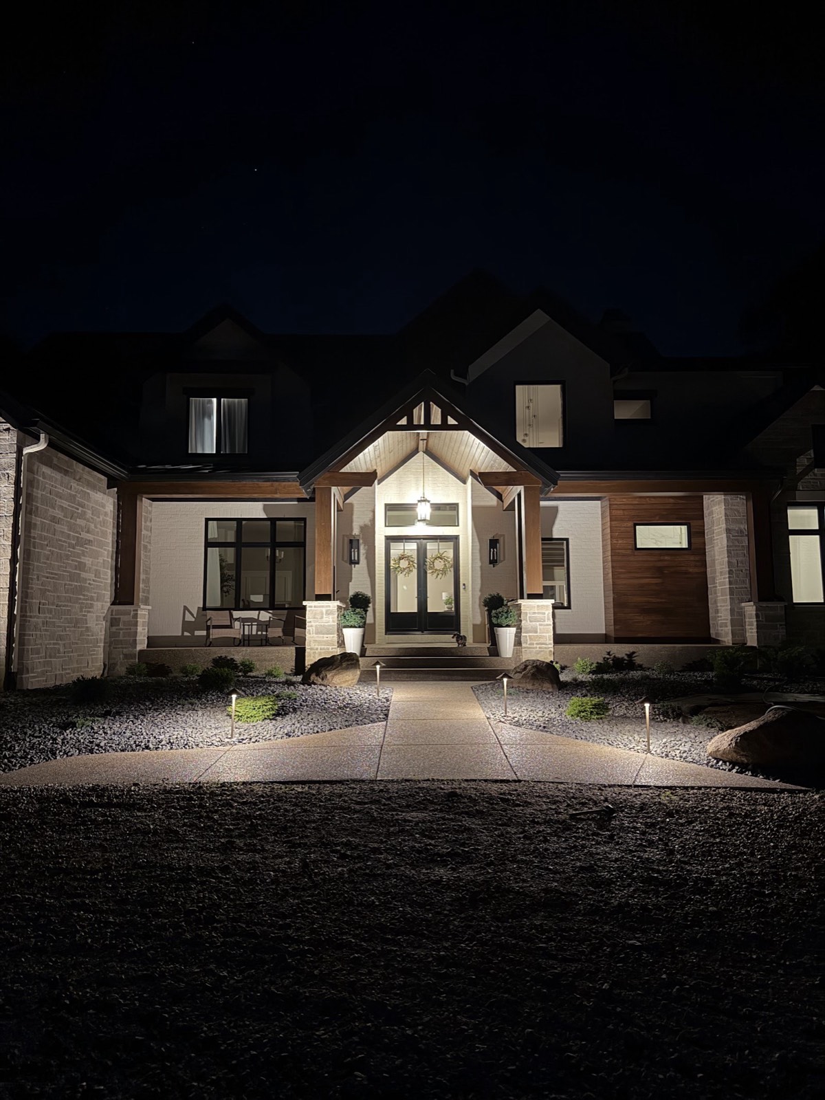 Dramatic nighttime view of a custom home entry with new path lights, rock beds, and boulders lining the front walkway.