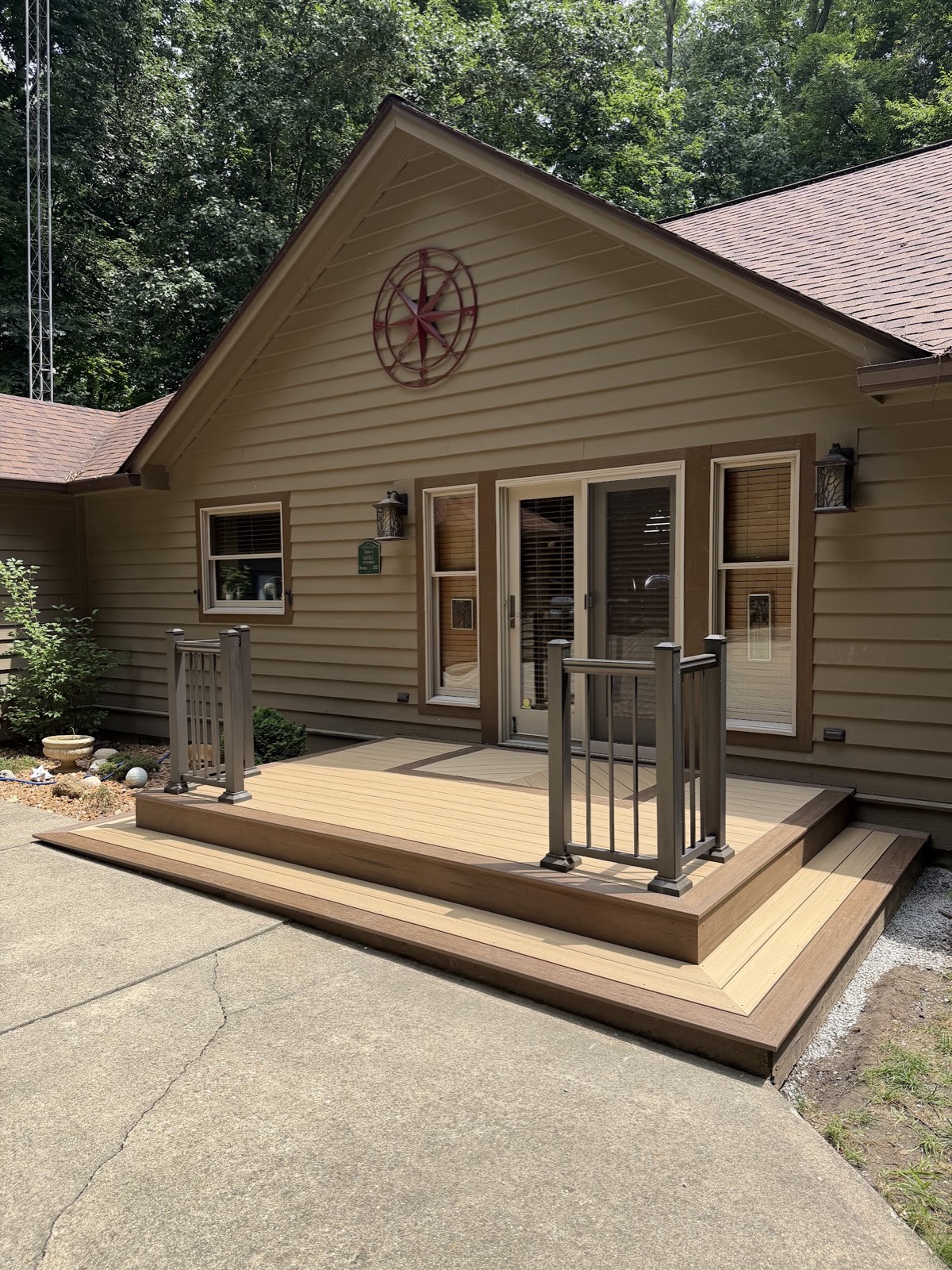 Wide view of a completed two-tone composite entry deck with wrap-around steps and railings on a gabled tan house.