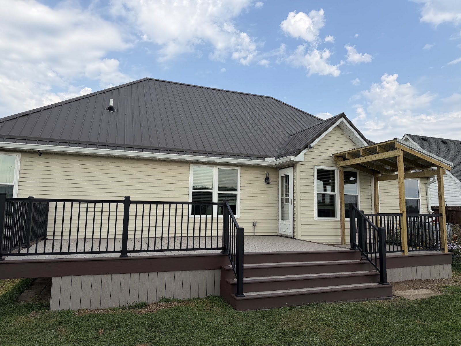 Completed composite deck with black aluminum railing, stairs, and a new cedar pergola on the back of a house.
