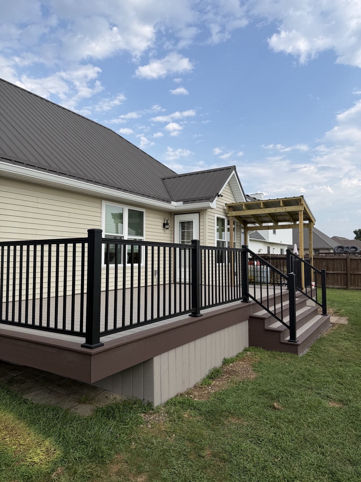 Completed composite deck with black aluminum railing, stairs, and a new pressure-treated covered pergola at the door.