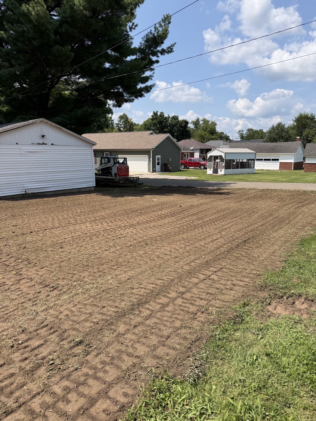 Backyard graded and tilled to bare dirt for lawn prep with a skid steer parked by the garage.